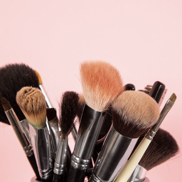 Diversos tipos de pincéis de maquiagem em um fundo rosa claro 