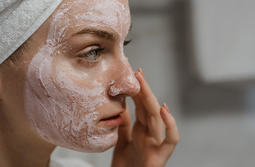 mulher branca olhando para frente enquanto espalha um dos produtos da rotina de skincare no rosto