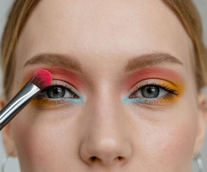 Uma mulher com um pincel de sombra passando uma maquiagem colorida nos olhos
