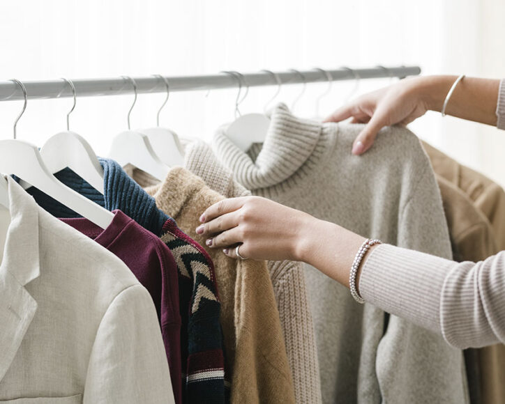 Uma mulher em frente a uma arara de roupas escolhendo uma peça de roupa de frio 