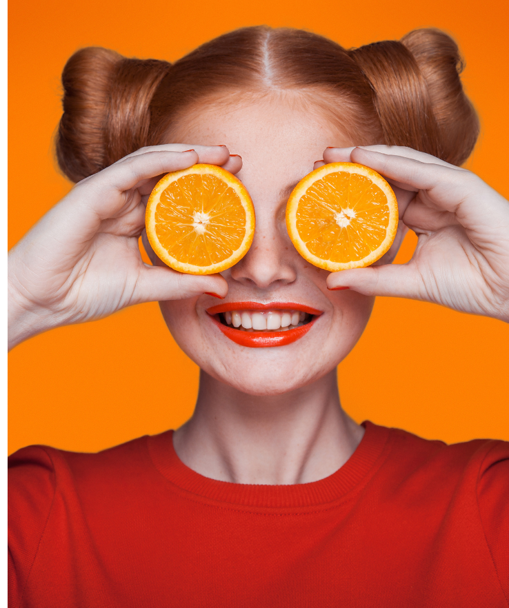 mulher com expressão sorridente segurando duas rodelas de laranja nos olhos